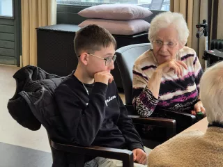 Een oudere dame en jonge basisschool jongen samen aan tafel in gesprek